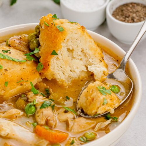 Slow cooker chicken and dumplings in a white bowl with a spoon in it, salt and pepper and parsley in the background