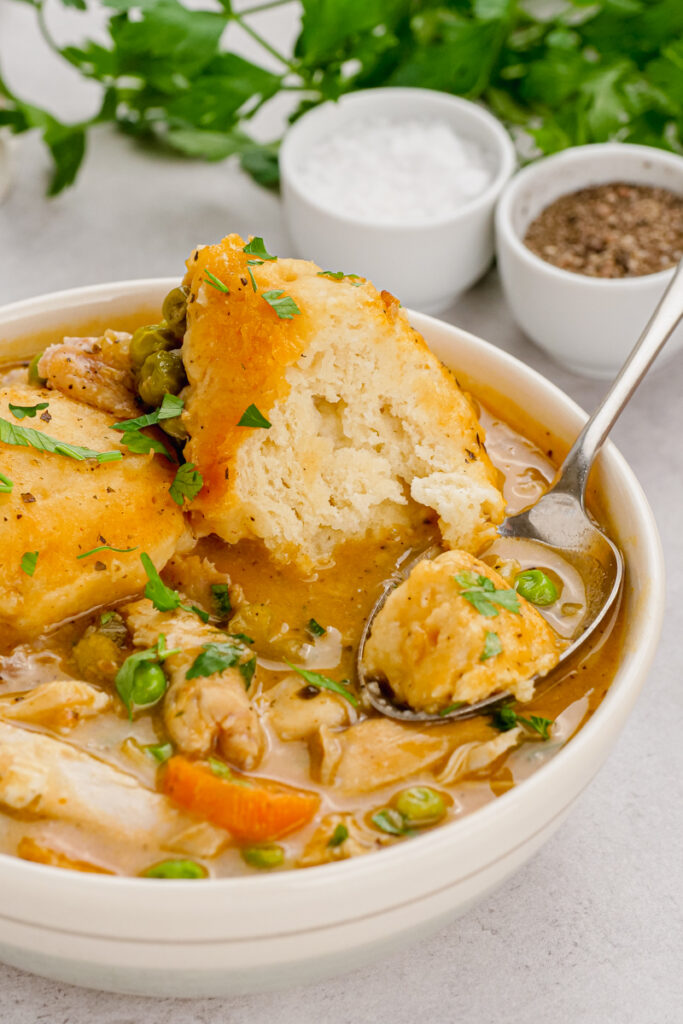 Slow cooker chicken and dumplings in a white bowl with a spoon in it, salt and pepper and parsley in the background