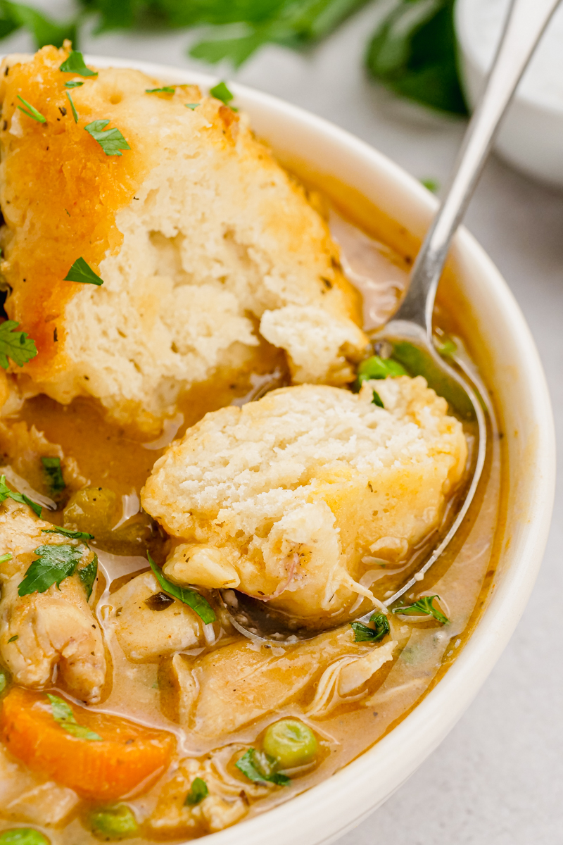 A white bowl with chicken and dumplings, a spoon scooping