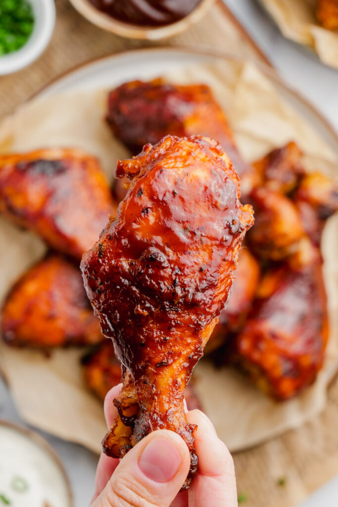 Slow Cooker BBQ Drumsticks in hand with more in the backround.