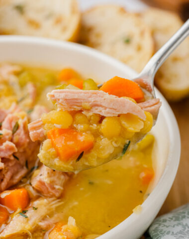 Split pea soup in white bowl with spoon in it with bread to the side