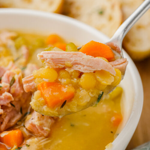 Split pea soup in white bowl with spoon in it with bread to the side