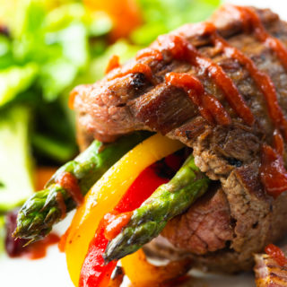 Steak roll ups- these low carb steak fajitas roll ups are on a white plate with a green salad in the background