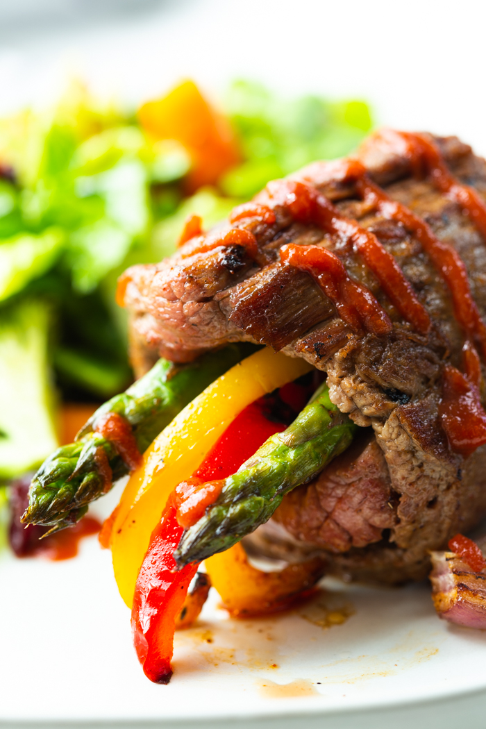 Steak roll ups- these low carb steak fajitas roll ups are on a white plate with a green salad in the background