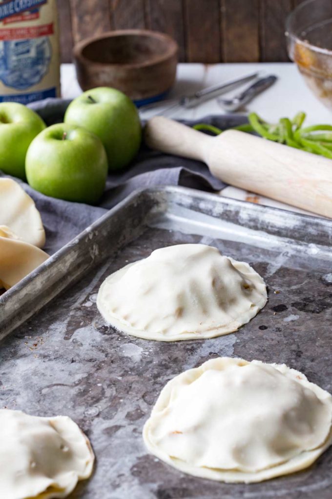 Add topping to mummy apple hand pies, apple pies made to look like mummies for a fun halloween treat