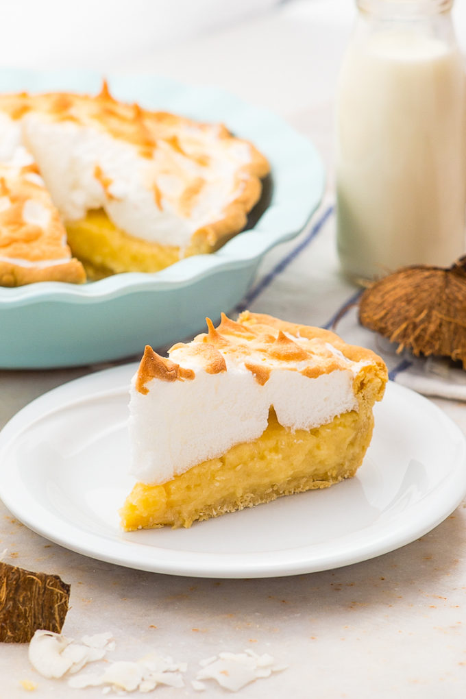Thick and creamy coconut cream pie topped with fluffy meringue with milk and coconut shells in the background