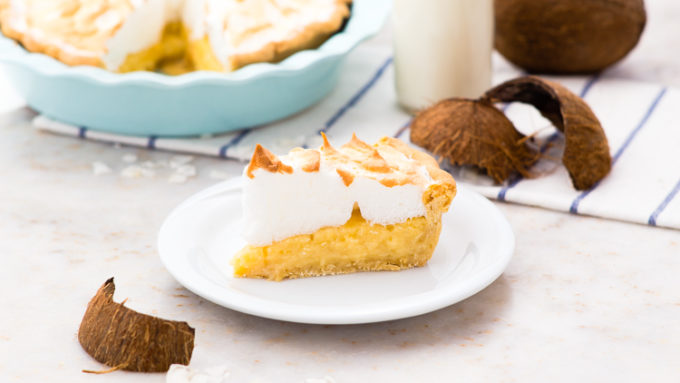 slice of coconut creme pie on a white plate with coconut shells in the foreground and back ground