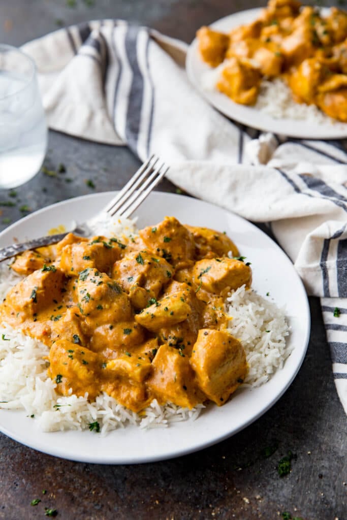 Delicious and easy Indian butter chicken over white rice on a white plate with a silver fork