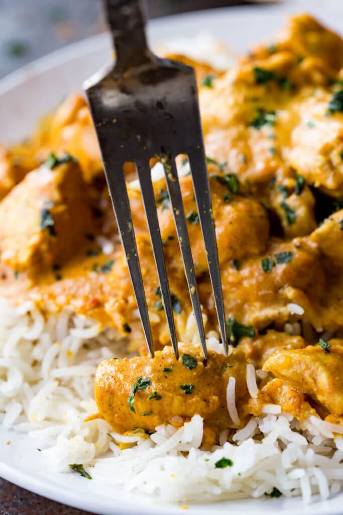 a fork with a piece of Indian butter chicken on it all over white rice