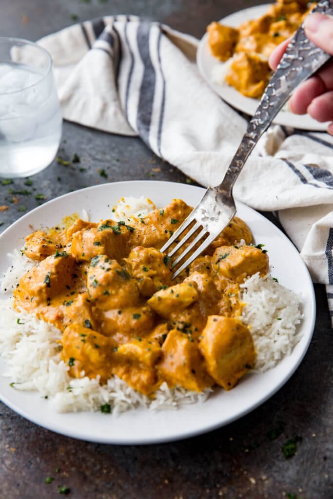 Indian Butter Chicken on white rice on a white plate with a silver fork