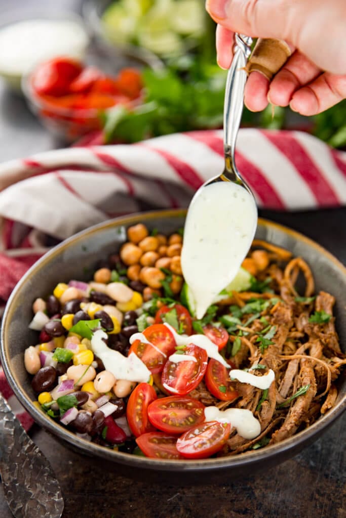 Adding dressing to a protein bowl made with pork and pulse