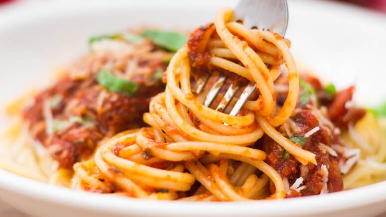 Homemade spaghetti sauce on top of noodles, twirled noodles on a fork