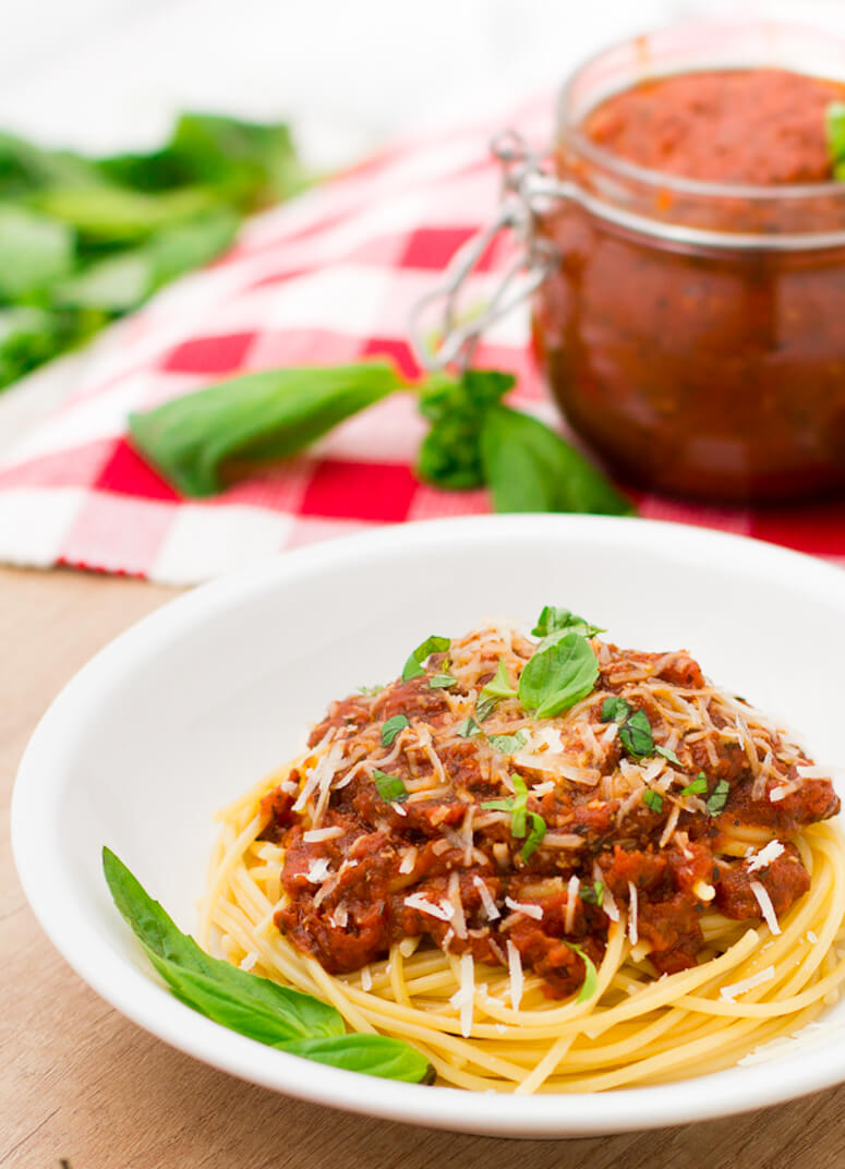 fresh spaghetti sauce on top of noodles in a white bowl with basil and parmesan as garnish 