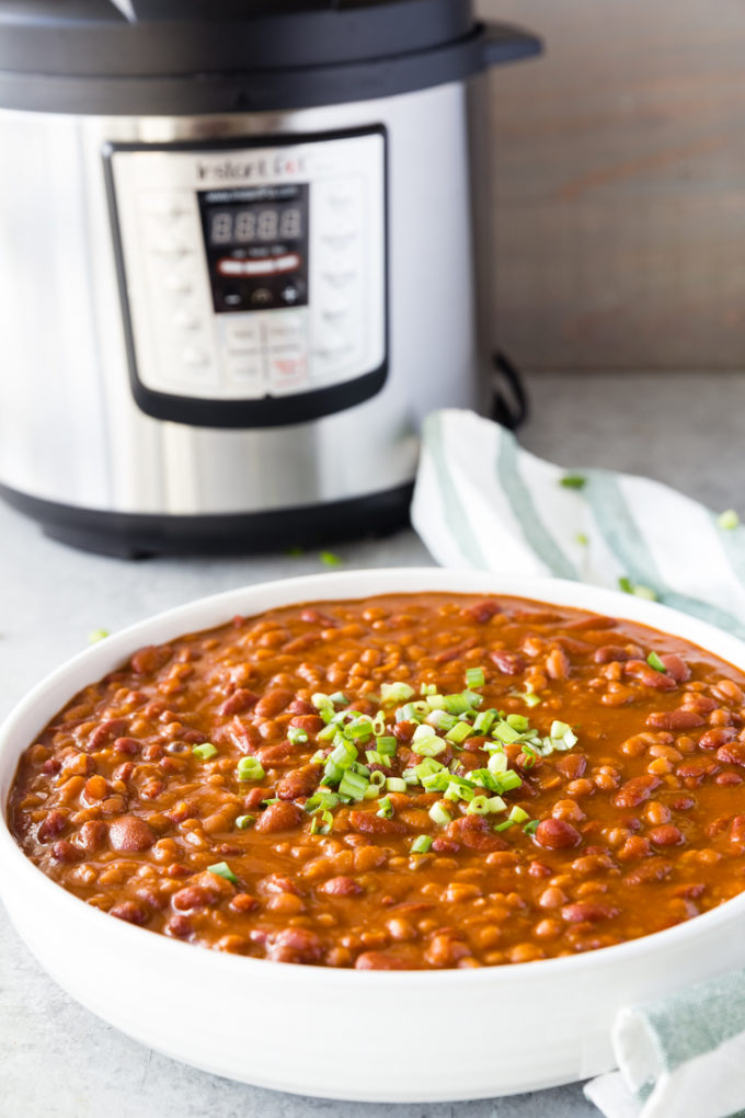 Instant Pot Baked Beans in a white bowl, with Instant Pot pressure cooker behind, garnished with green onion