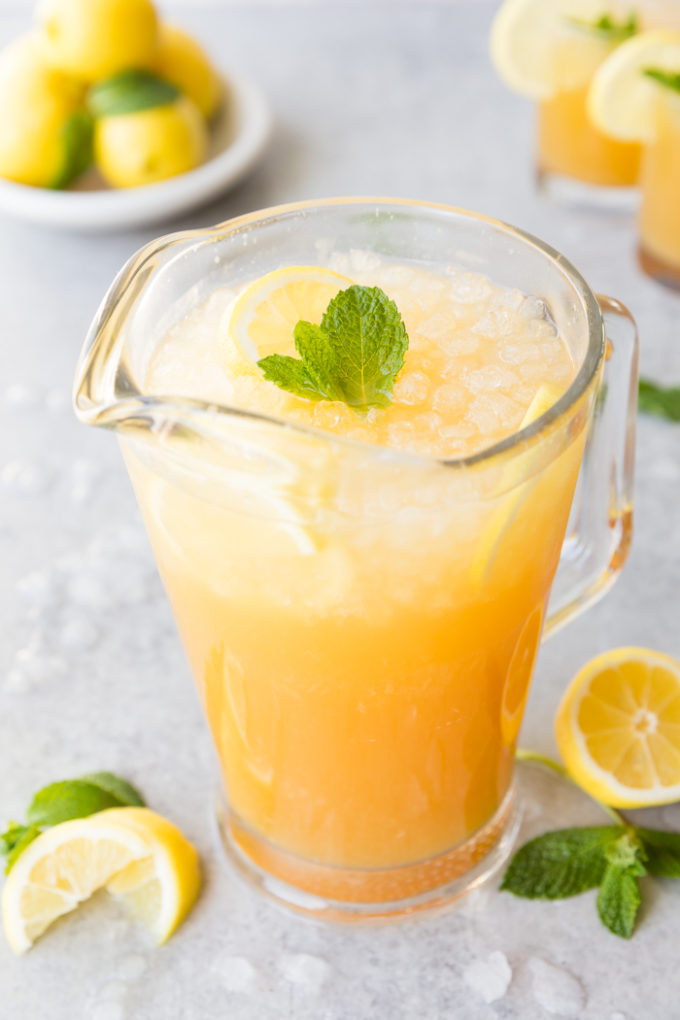 A glass pitcher of Mango Black Tea Lemonade with mint and lemon garnish
