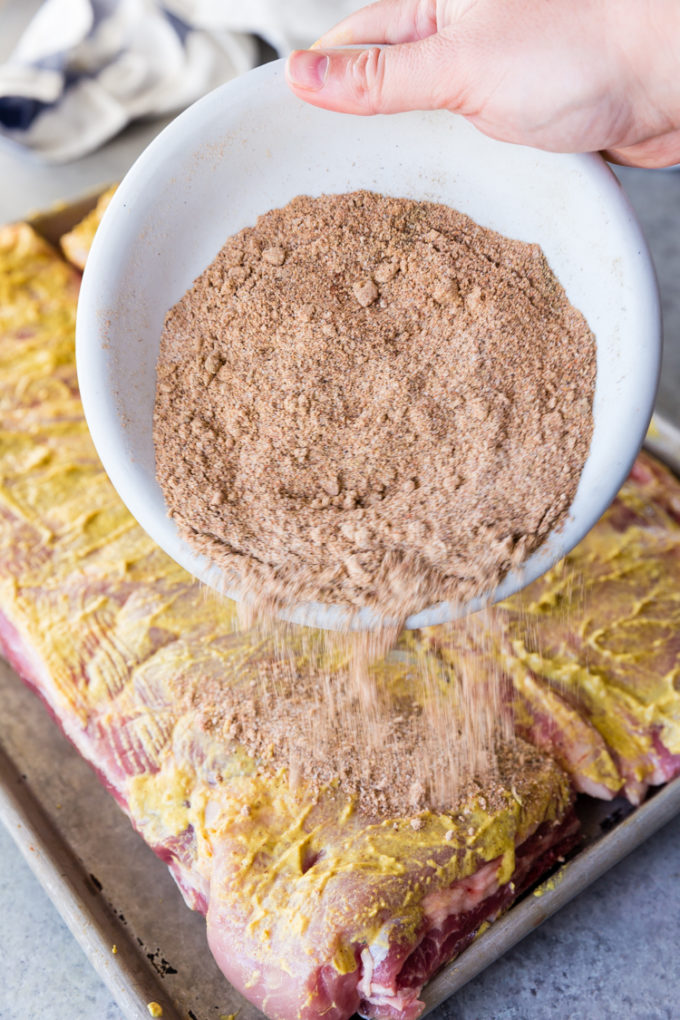Pouring spice mixture on to ribs covered in mustard. 