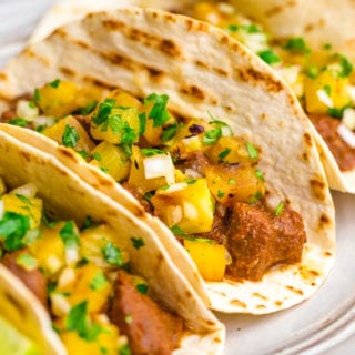 Three tacos al pastor with pineapple pico on top and lime garnish