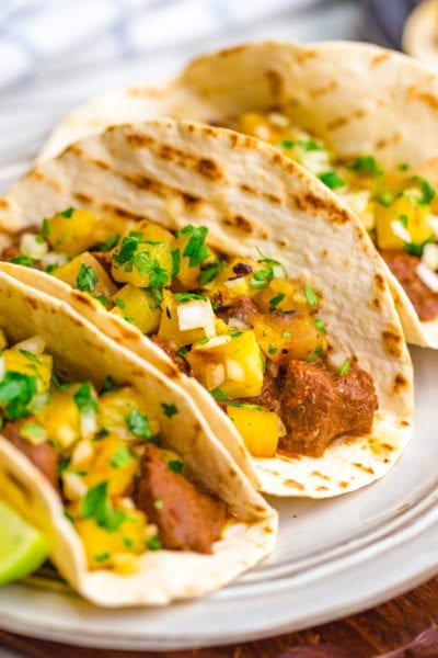 Three tacos al pastor with pineapple pico on top and lime garnish