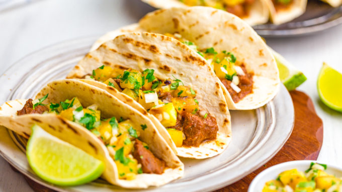Tacos al pastor with three tacos on a plate, with lime wedges