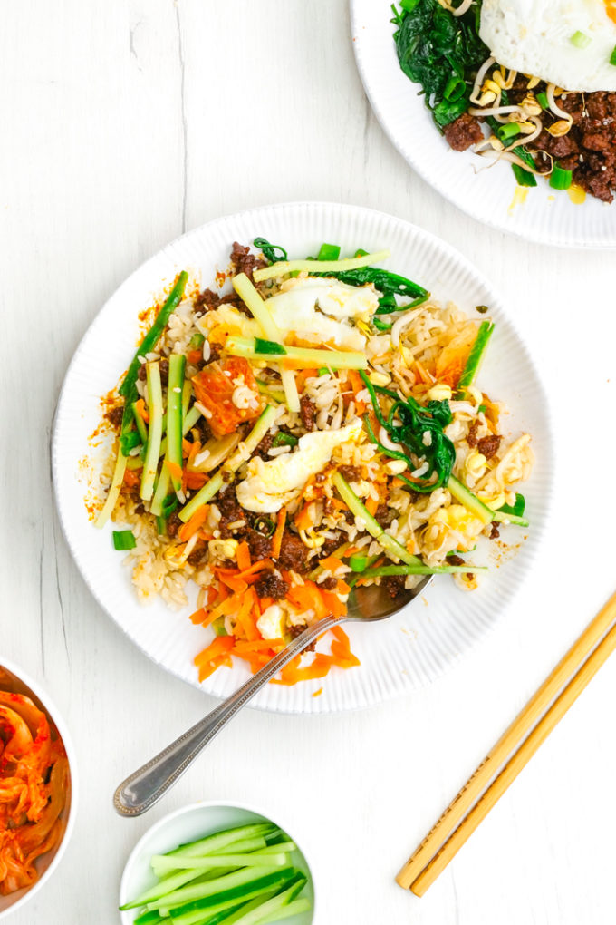 A mixed up Korean Beef Bibimbap on a white plate with chopsticks and a fork