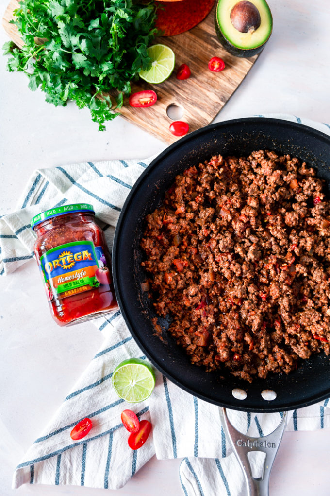 Easy Ground Beef Tacos, a skillet of ground beef taco meat, and a cutting board with taco fixings. 