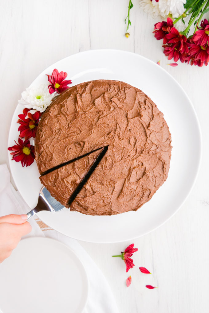 A top down view of a chocolate cake with a single slice cut, and a spatula pulling it out.