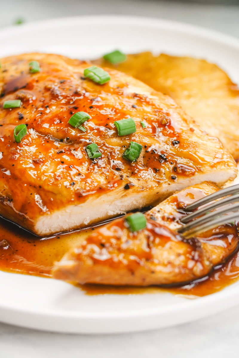 A white plate with a piece of teriyaki chicken, garnished with green onion