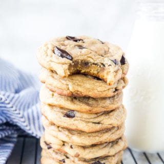 A stack of Traeger Smoked Chocolate Chip Cookies, with a glass of milk, a napkin, and a cooling rack.
