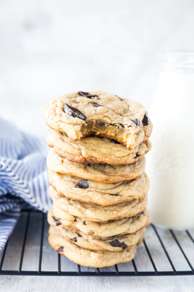 A stack of Traeger Smoked Chocolate Chip Cookies, with a glass of milk, a napkin, and a cooling rack.