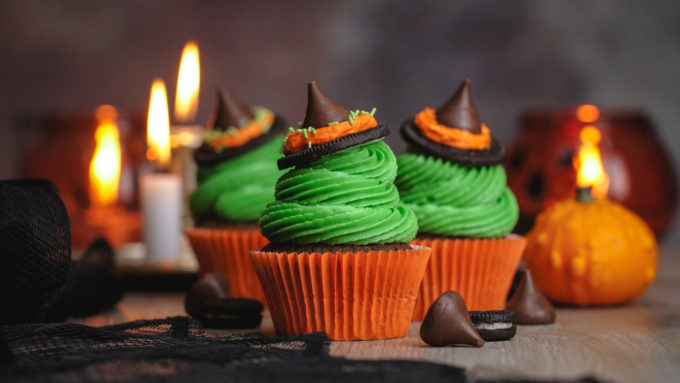 3 witch hat cupcakes with candles and a pumpkin in the background