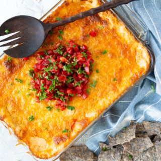 Cheesy Corn Dip- in a casserole dish, topped with fresh tomatoes and cilantro and served with tortilla chips