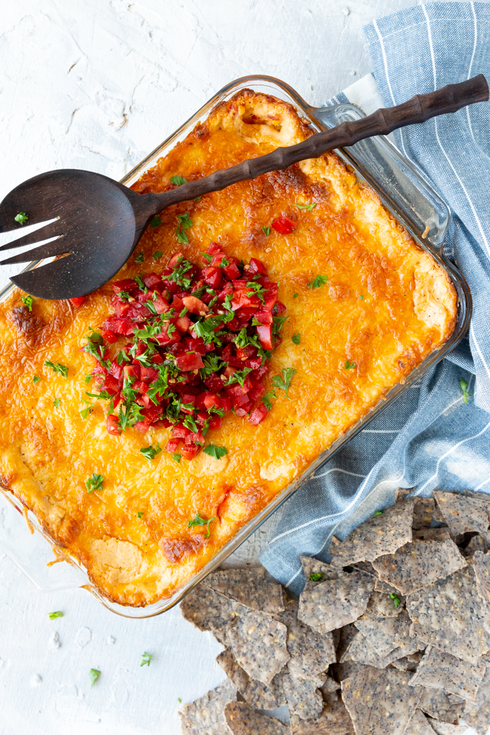 Cheesy Corn Dip- in a casserole dish, topped with fresh tomatoes and cilantro and served with tortilla chips