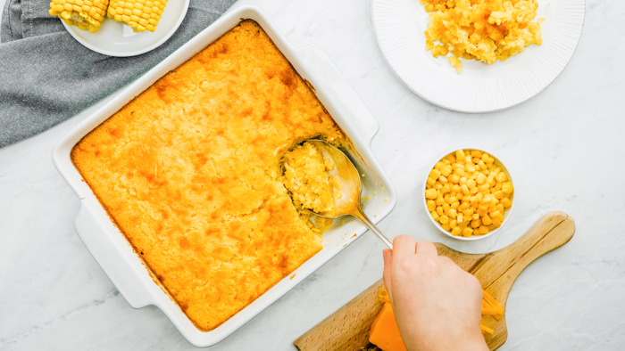 A casserole dish of corn casserole, a bit serving spoon, and a plate