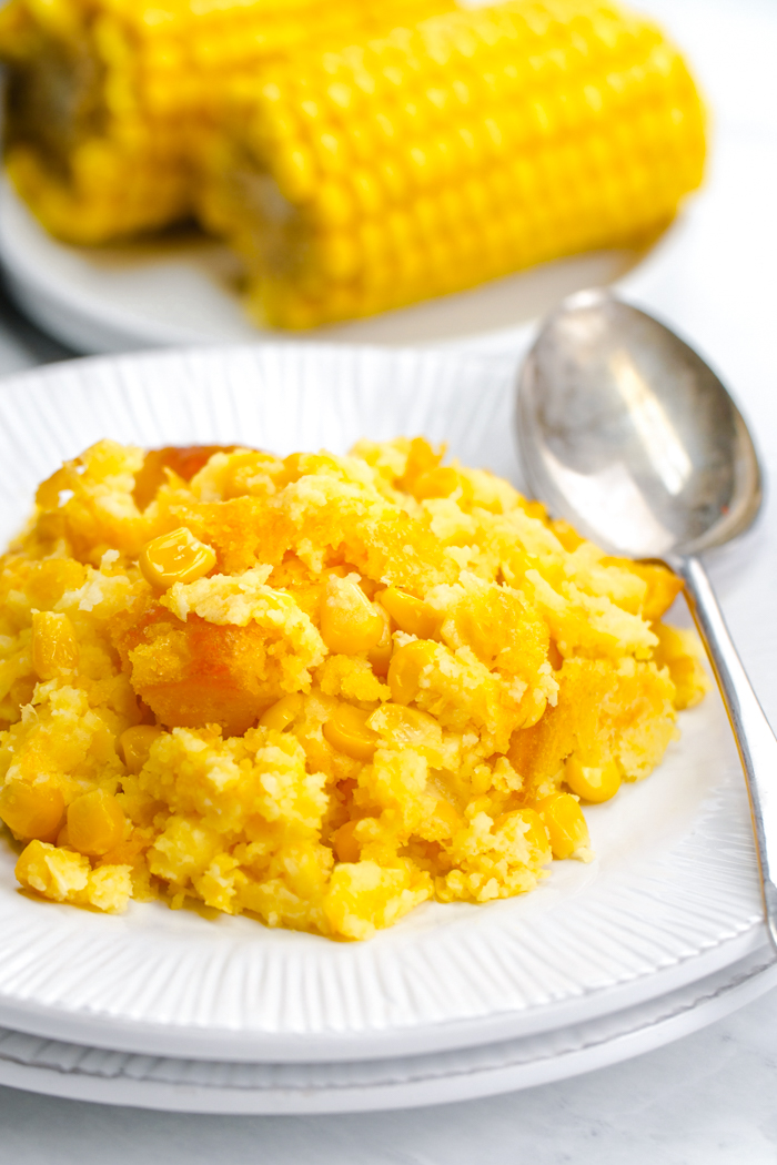 A delicious corn casserole, on a white plate with a silver spoon