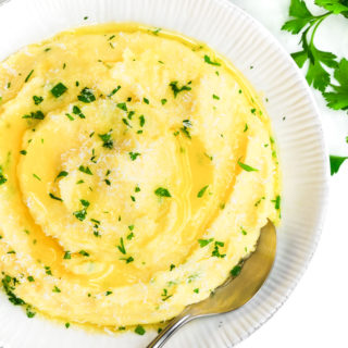 Herb Butter Mashed Potatoes in a white bowl with a silver spoon and herb garnish