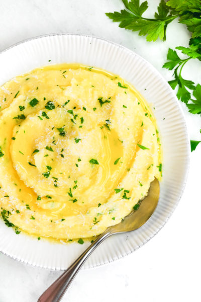 Herb Butter Mashed Potatoes in a white bowl with a silver spoon and herb garnish