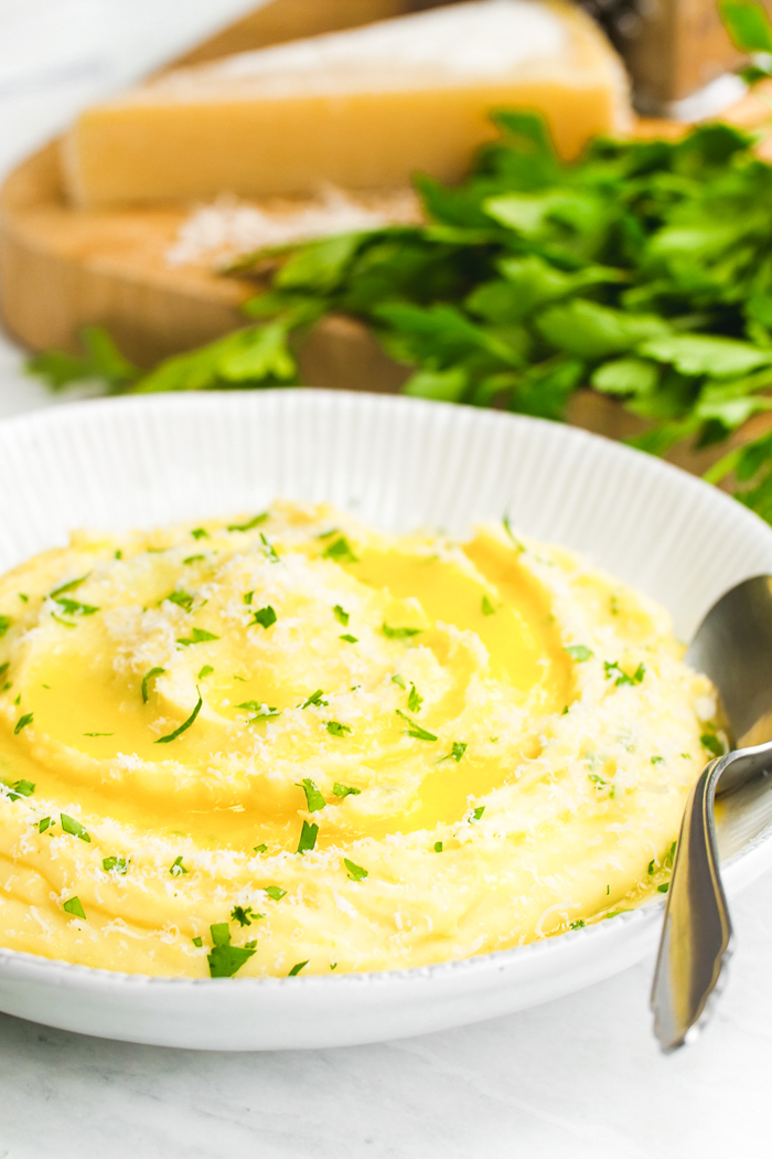 A white bowl full of mashed potatoes topped with herbs and butter. Creamy and delicious mashed potatoes