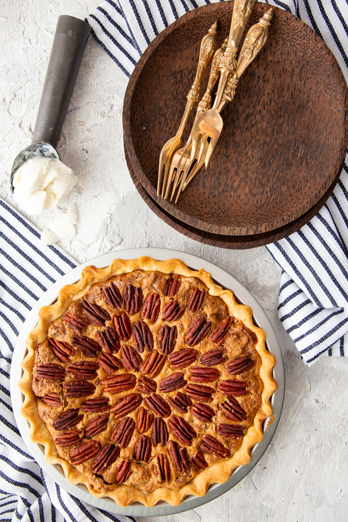 Pecan Pie recipe with a whole pie, brown plates, gold forks, and ice cream