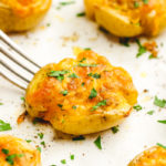 A tray with 5 smashed potatoes, a fork picking up the center potatoes which is garnished with parsley
