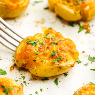 A tray with 5 smashed potatoes, a fork picking up the center potatoes which is garnished with parsley