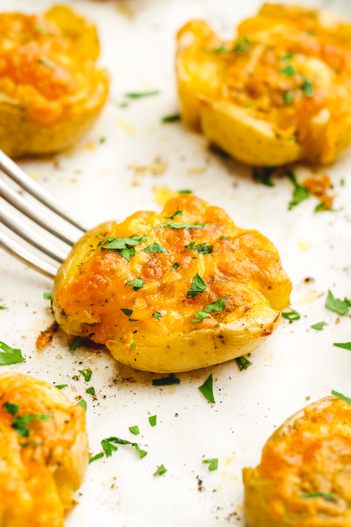 A tray with 5 smashed potatoes, a fork picking up the center potatoes which is garnished with parsley