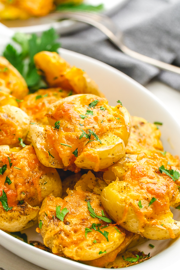 A tray of smashed potatoes with herb garnish, napkin and fork in background