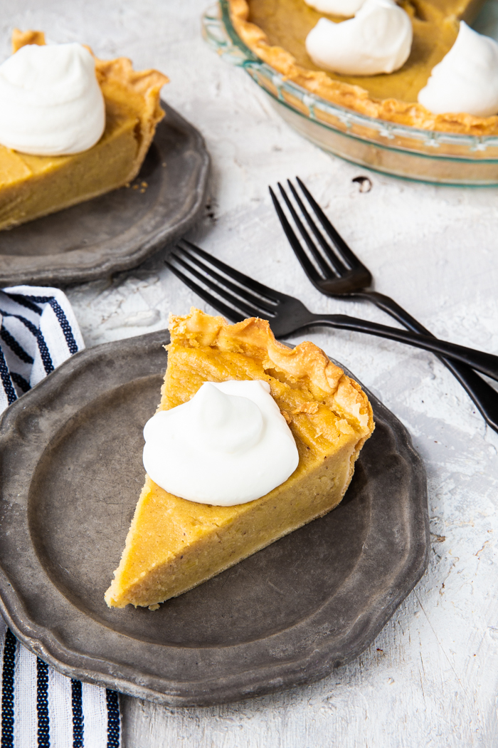 A plate topped with sweet potato pie, two forks crossed, a pie plate, and whip cream dollops on top of the pie slices