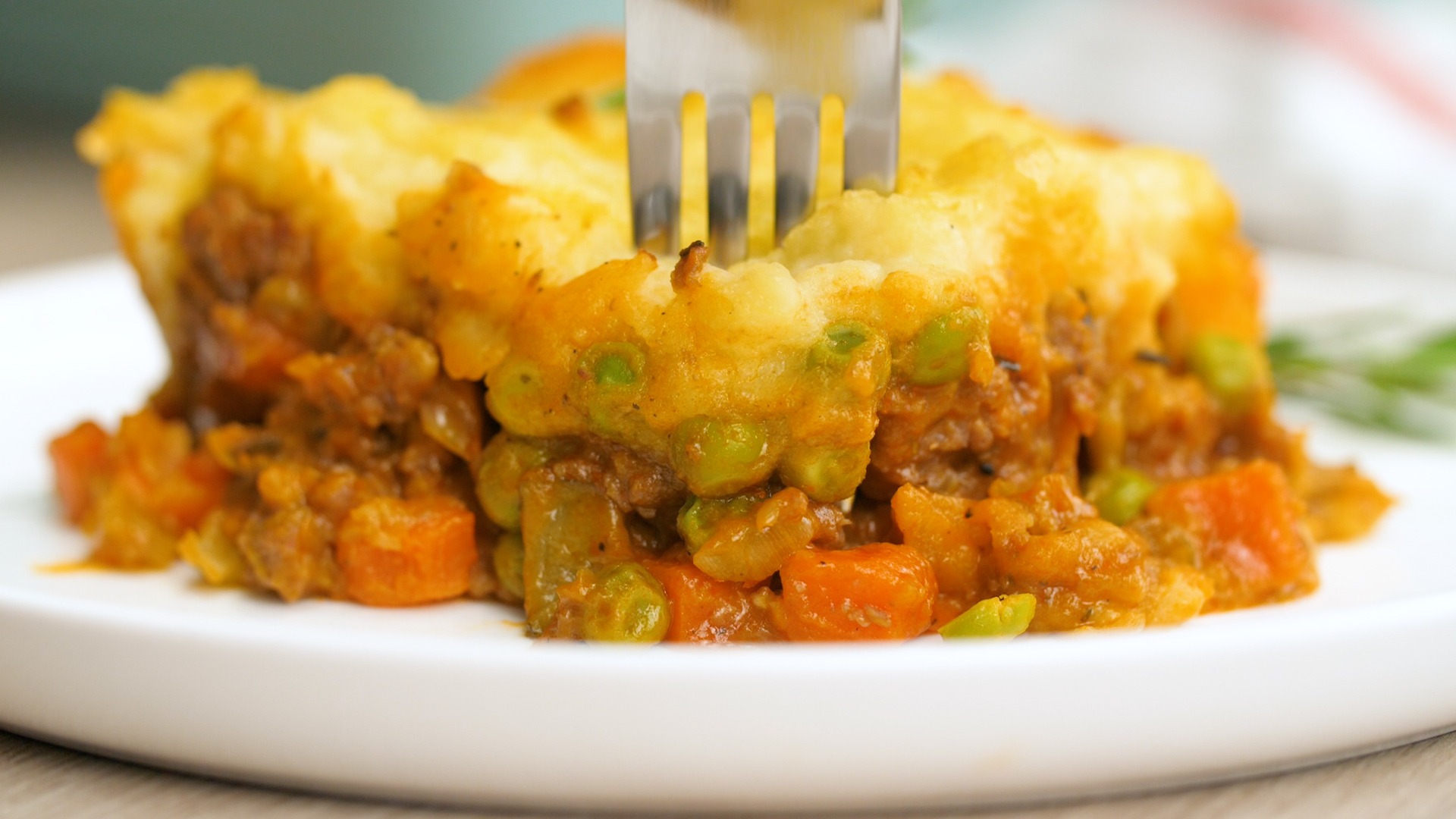 A front view of some shepherd's pie, with the ground lamb filling, and vegetables and potato layer, a fork sticking in the top