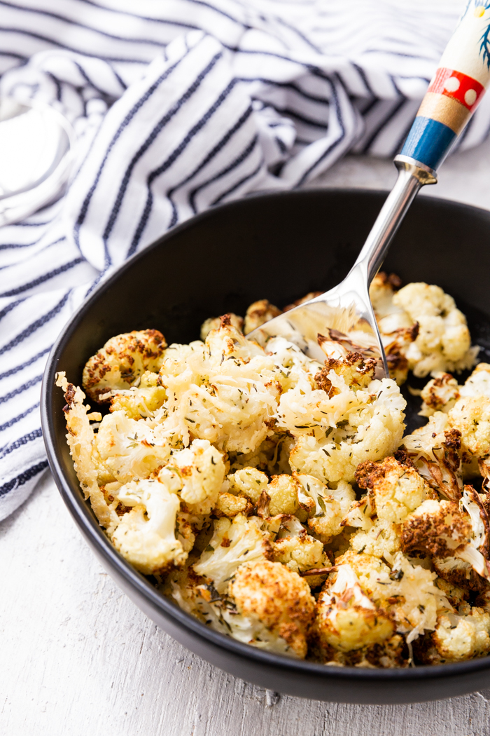 Air fryer roasted cauliflower in a black bowl with a spoon and striped napkin