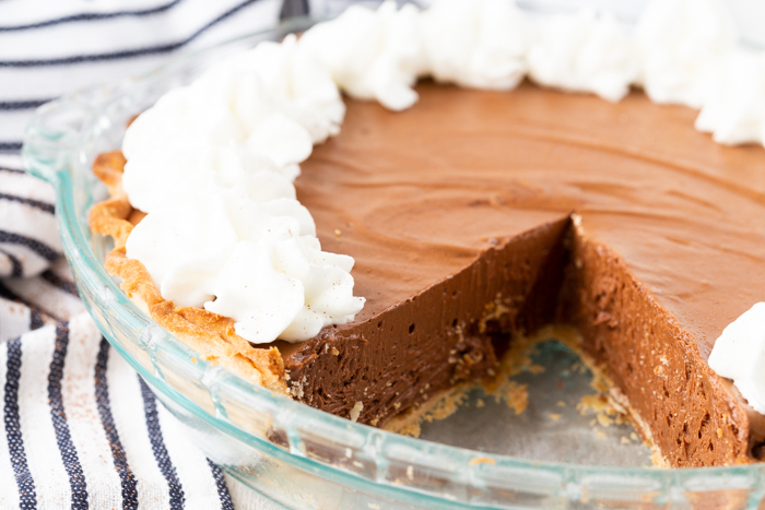 A whole chocolate pie, a slice out of the pie, and some whipped cream.