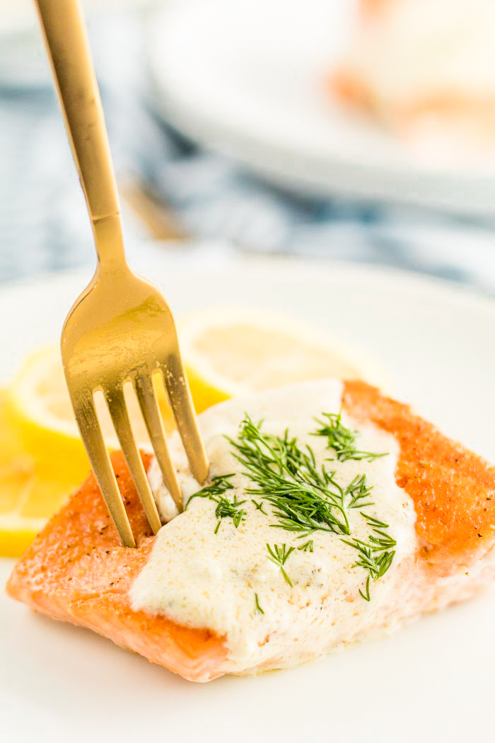 A white plate with creamy lemon dill sauce on salmon