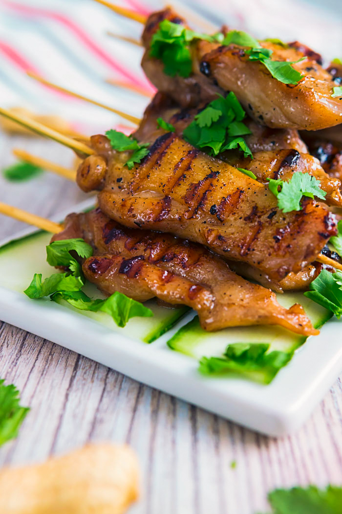 A white platter loaded with chicken satay skewers garnished with fresh cilantro. 