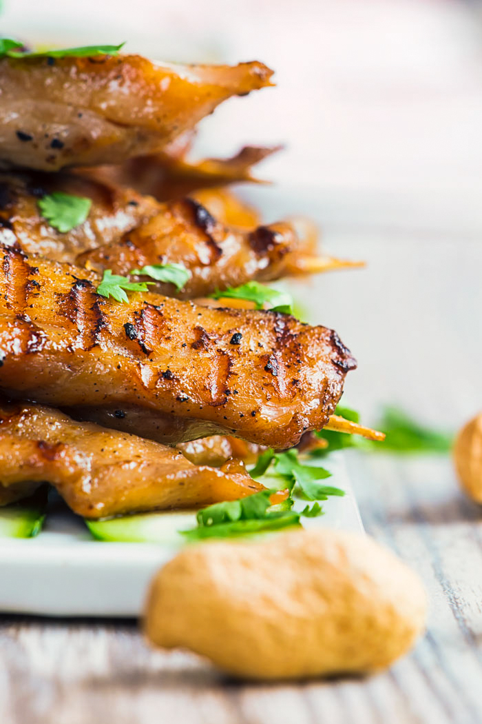 Chicken satay on a white serving plate with a peanut in front for the peanut dipping sauce