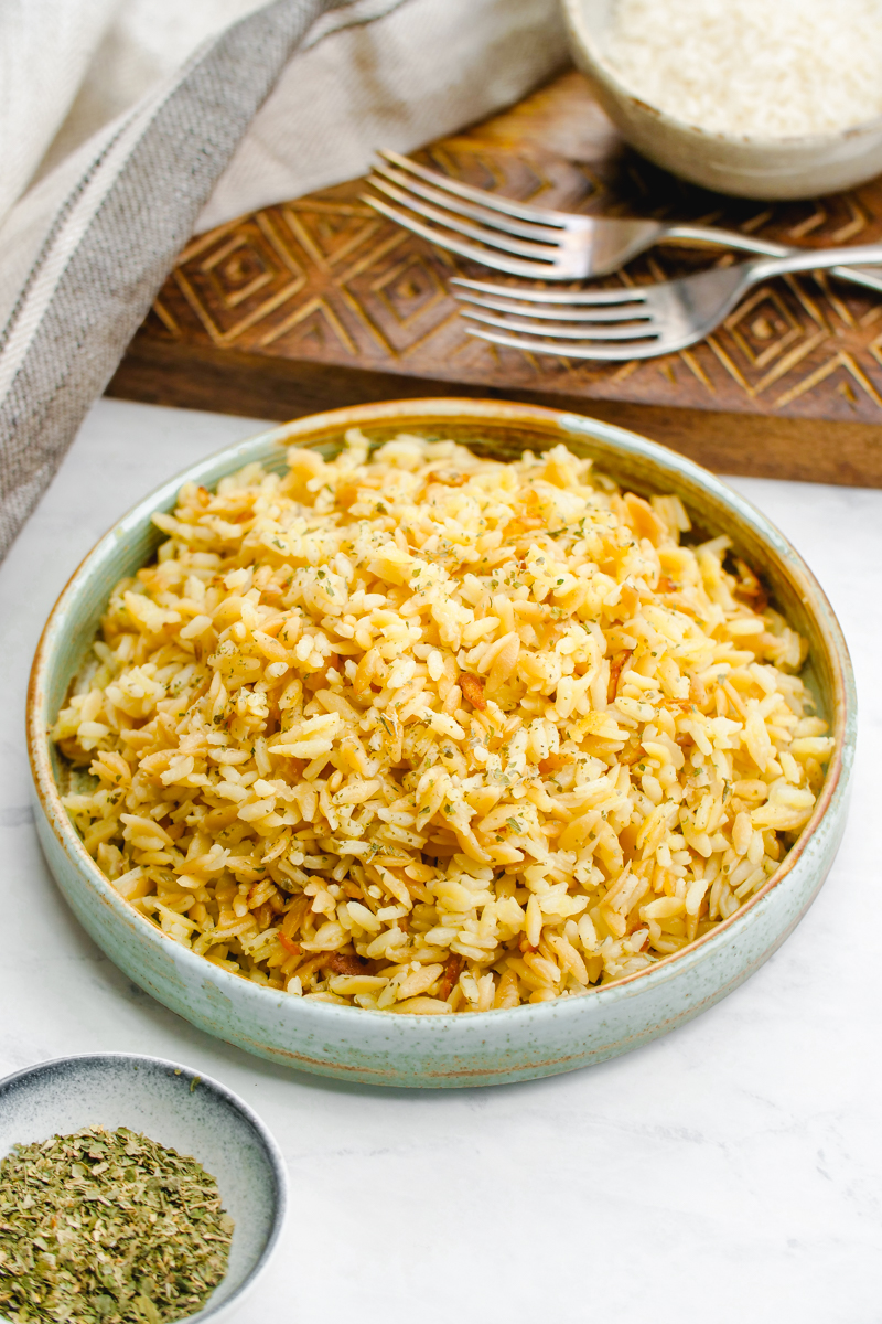 A beautiful bowl of rice pilaf with a cutting board and forks behind it